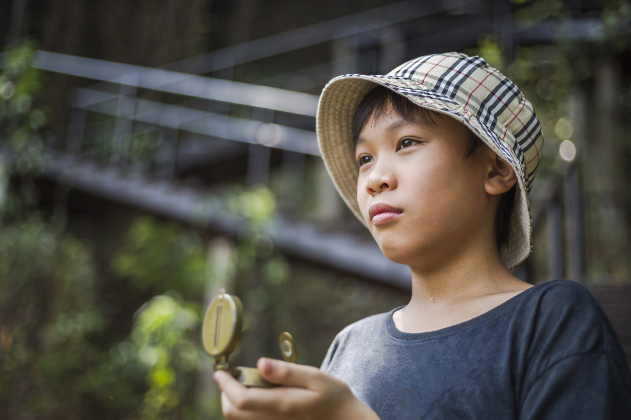  Un garçon asiatique s'oriente à l'aide d'une boussole dans la forêt