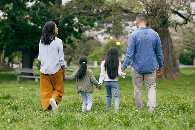 A family walks outdoors, holding hands and looking forward.