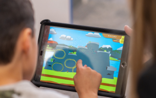 A child and an adult looking over the Dino Island video game on a tablet.