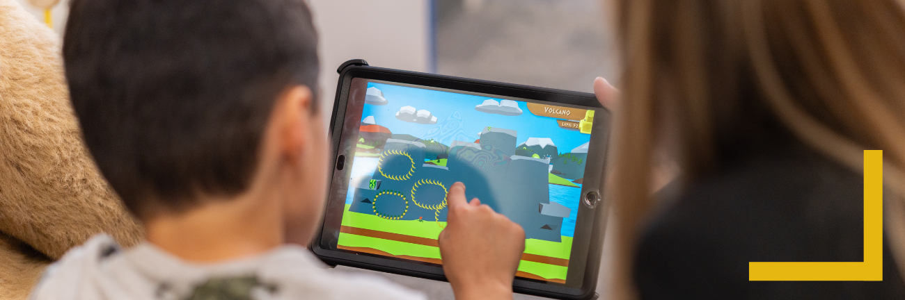 A child and an adult looking over the Dino Island video game on a tablet.