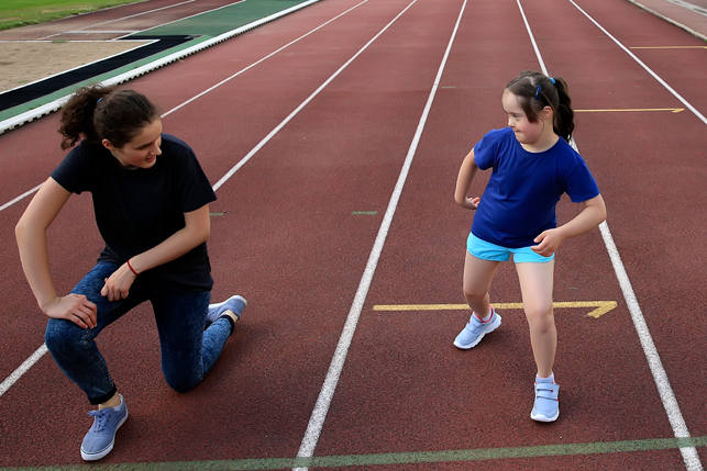 A child with Down Syndrome and her coach get into starting position on a racetrack.
