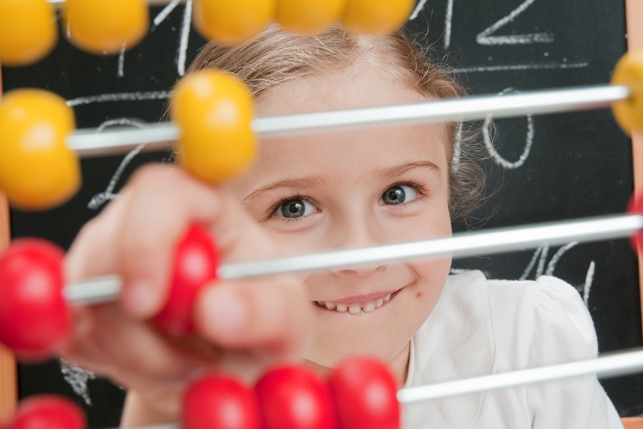 A smiling child manipulates an abacus. Behind her, there are math equations on a blackboard.