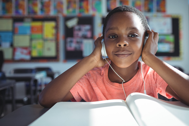 A child with a peaceful expression wears earphones in the classroom.