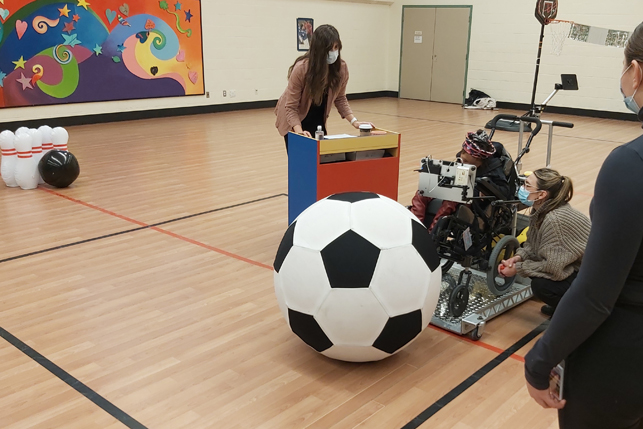 A child uses a BCI cap to propel an electric wheelchair towards a ball.