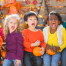 A diverse group of children are laughing and shouting while holding pumpkins. There is a text overlay that says "Helping all kids live their best lives."