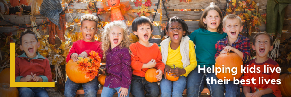 A diverse group of children are laughing and shouting while holding pumpkins. There is a text overlay that says "Helping all kids live their best lives."