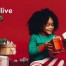 Two children in festive pajamas exchange gifts by a Christmas tree with stacked presents. Warm, joyful atmosphere. Text reads "Helping all kids live their best lives."