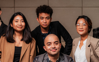 A diverse group of six people in professional attire pose confidently against a neutral office background. They convey a sense of teamwork and positivity.