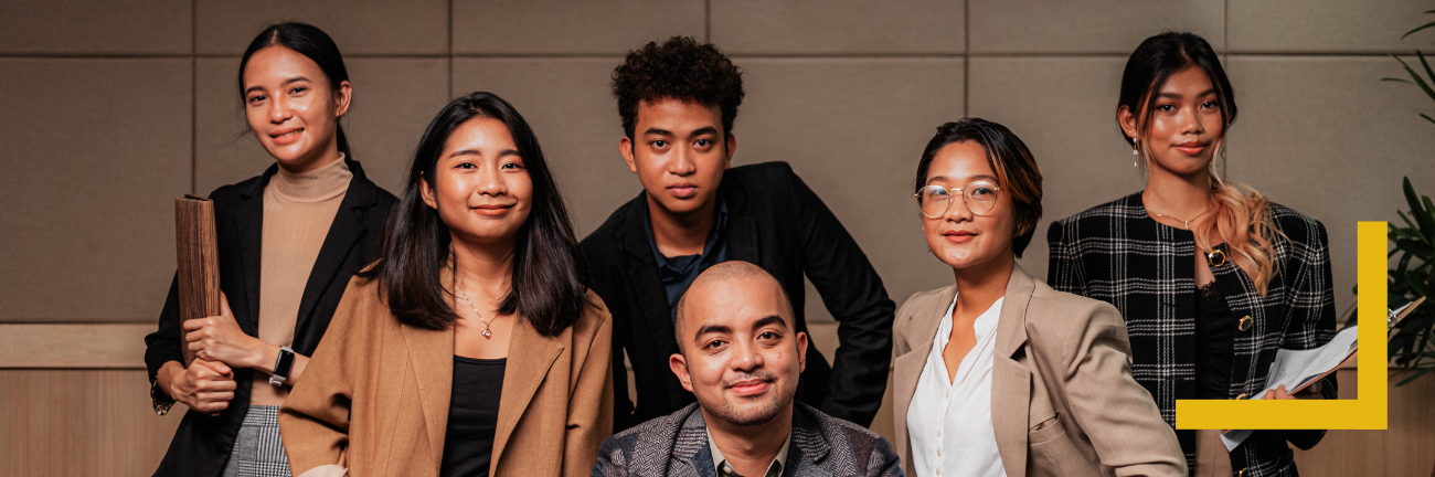 A diverse group of six people in professional attire pose confidently against a neutral office background. They convey a sense of teamwork and positivity.