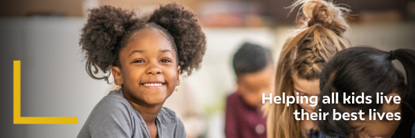 Smiling young girl with curly hair in a classroom setting, surrounded by other children. Text reads, "Helping all kids live their best lives."