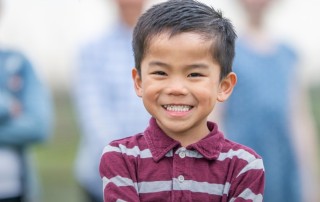 Smiling young boy in a striped shirt stands confidently in the foreground with a blurred group of diverse children behind him, conveying joy and togetherness.